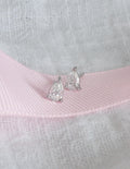 Pair of silver teardrop earrings on a textured pink and gray background