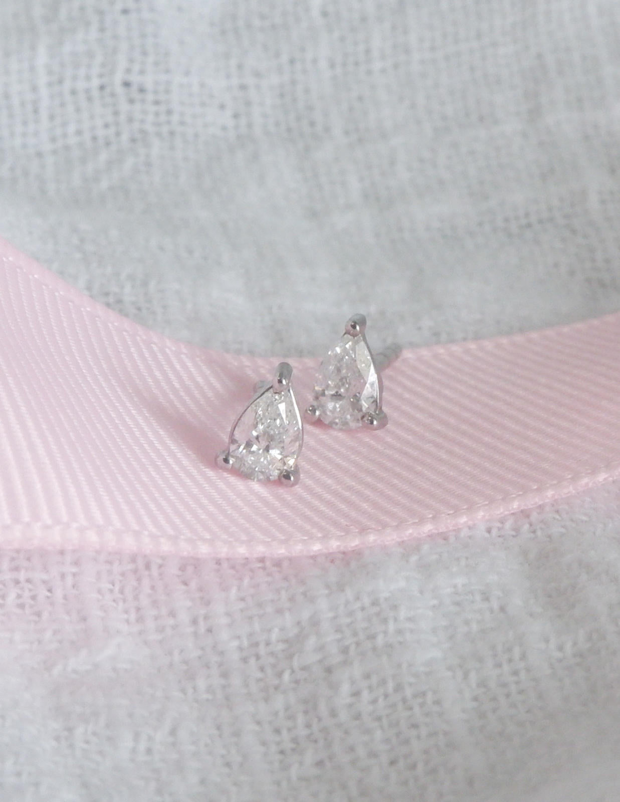 Pair of silver teardrop earrings on a textured pink and gray background